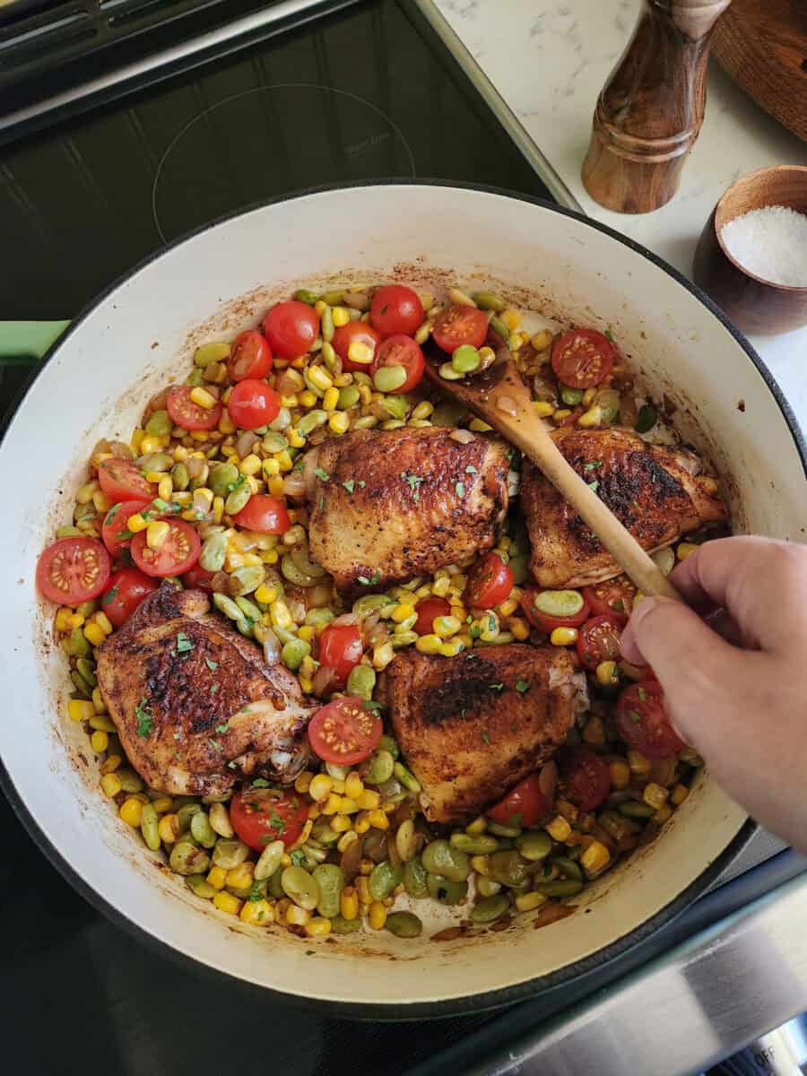 Stirring summer succotash in a skillet with chicken thighs.