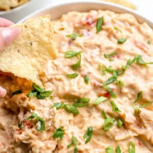 Dipping a tortilla chip into a bowl of Crockpot chicken queso.