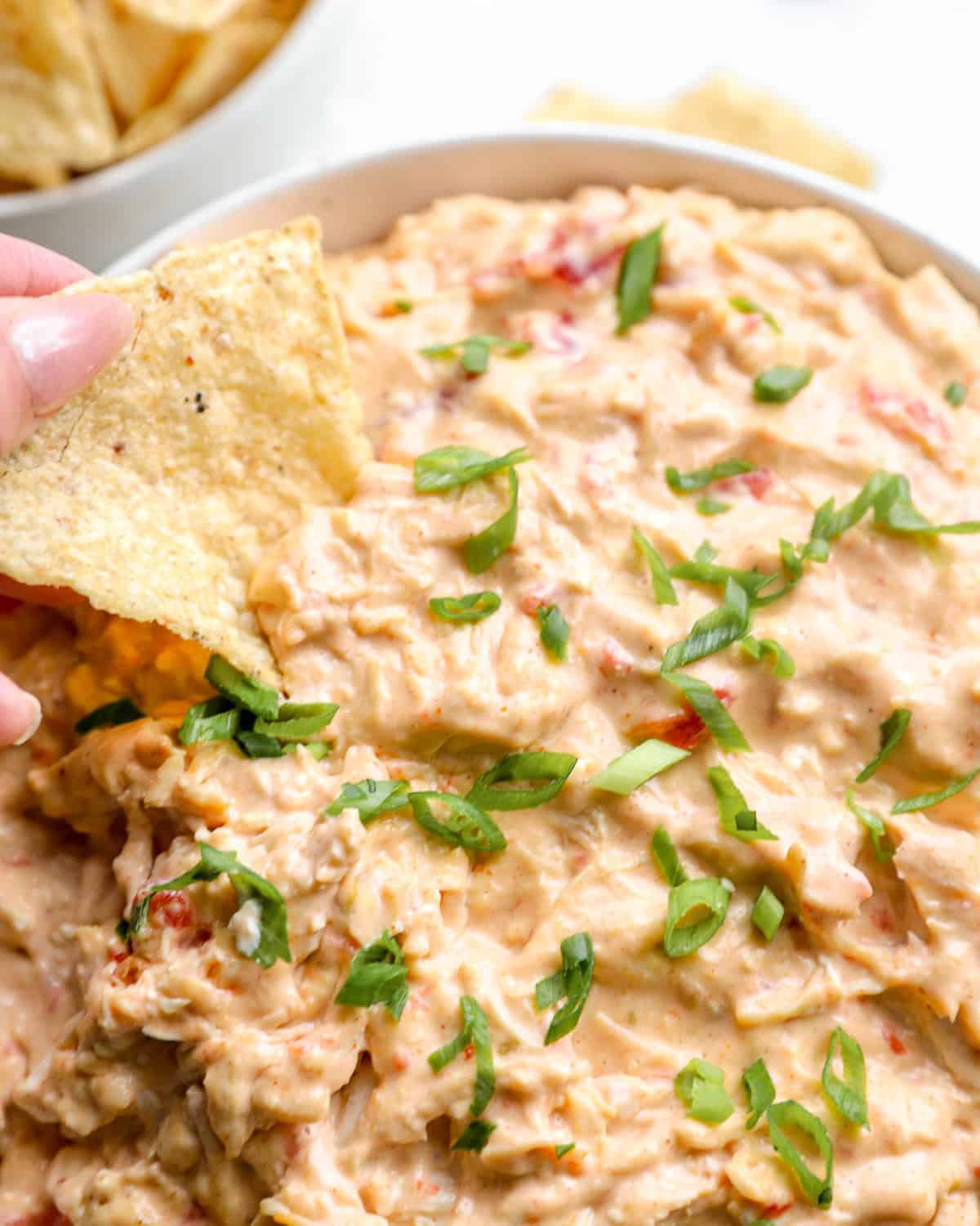 Dipping a tortilla chip into a bowl of Crockpot chicken queso.