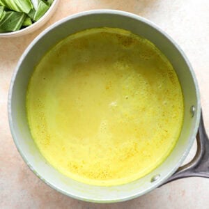 Golden coconut milk mixture with chicken broth, ginger and turmeric, in a saucepan.