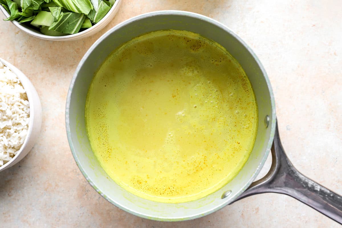 Golden coconut milk mixture with chicken broth, ginger and turmeric, in a saucepan.