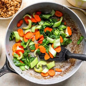 Sautéing carrots and bok choy in a skillet.