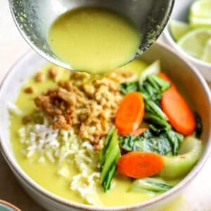 Pouring ginger and turmeric coconut broth over a bowl of ground chicken and rice.