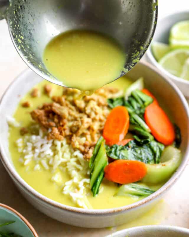 Pouring ginger and turmeric coconut broth over a bowl of ground chicken and rice.