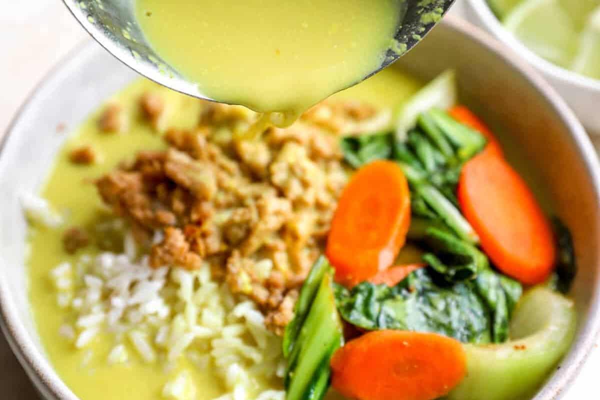 Pouring ginger and turmeric coconut broth over a bowl of ground chicken and rice.