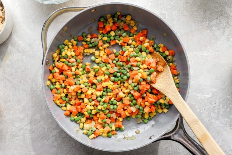 Stirring frozen mixed vegetables in a pan.