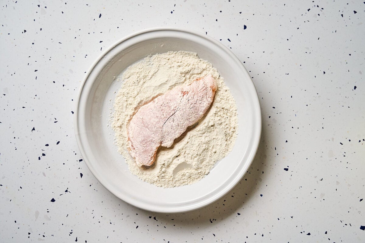 Chicken dredged in flour on a plate.