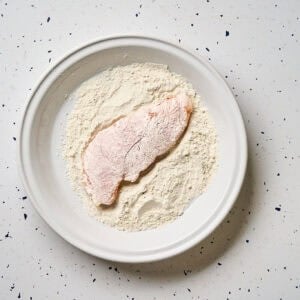 Chicken dredged in flour on a plate.
