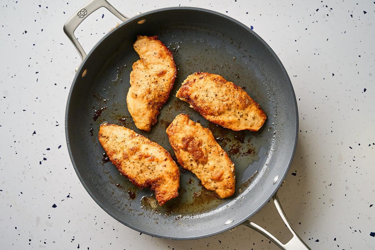 Chicken cutlets cooking in a pan.