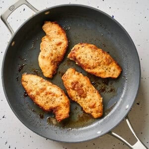 Chicken cutlets cooking in a pan.
