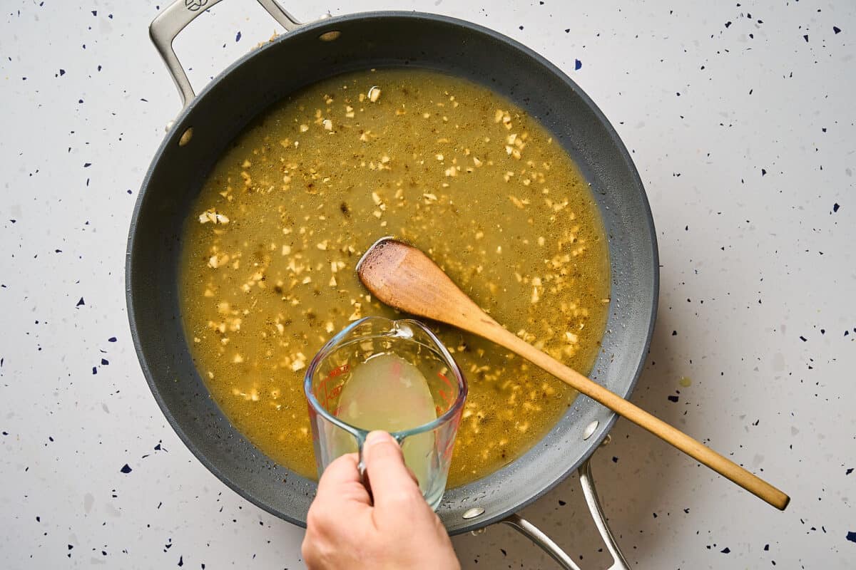 Pouring chicken broth into a skillet to deglaze.