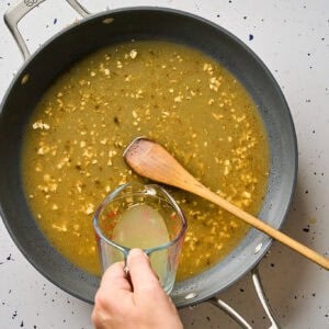Pouring chicken broth into a skillet to deglaze.