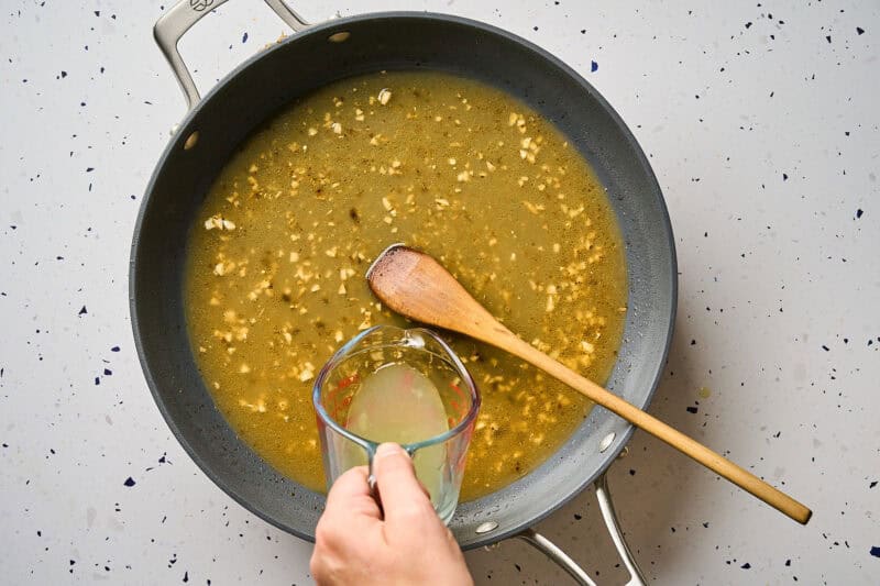 Pouring chicken broth into a skillet to deglaze.