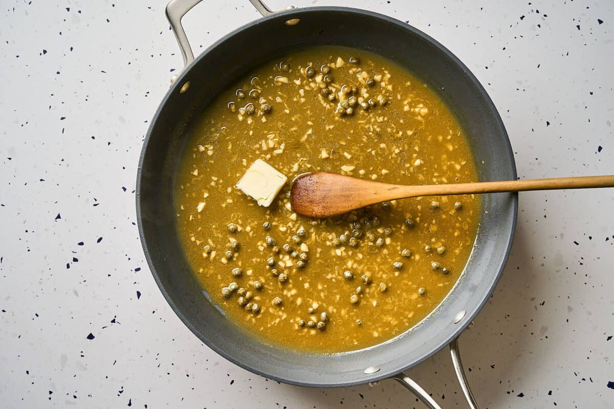Stirring a cube of butter into a pan of piccata sauce.
