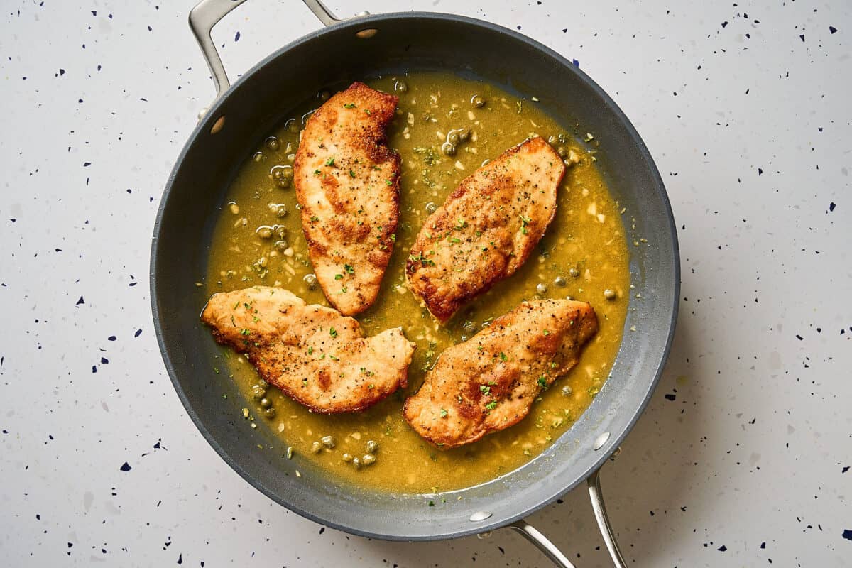 Chicken cutlets in a skillet with lemon piccata sauce.