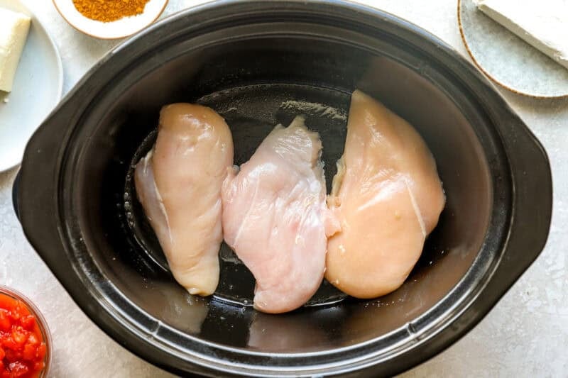 Raw chicken breasts place inside of a slow cooker.