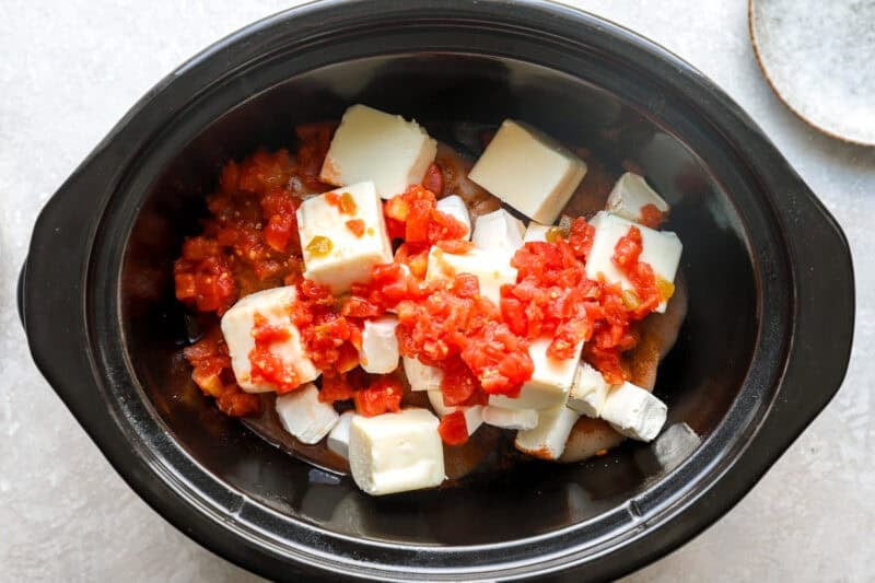 Rotel and cubes of cream cheese added to a slow cooker.