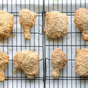 Breadcrumb coated chicken thighs, legs, and drumsticks lined up on a wire rack, on a baking sheet.