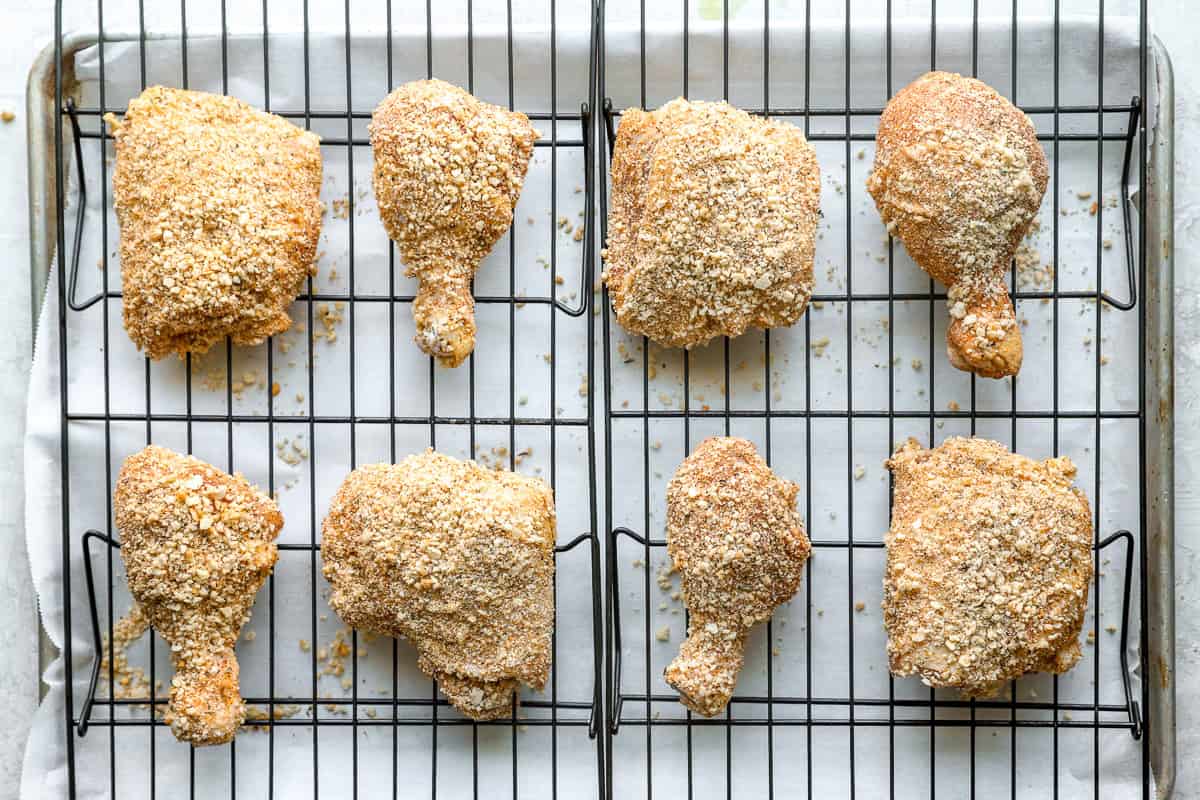 Breadcrumb coated chicken thighs, legs, and drumsticks lined up on a wire rack, on a baking sheet.