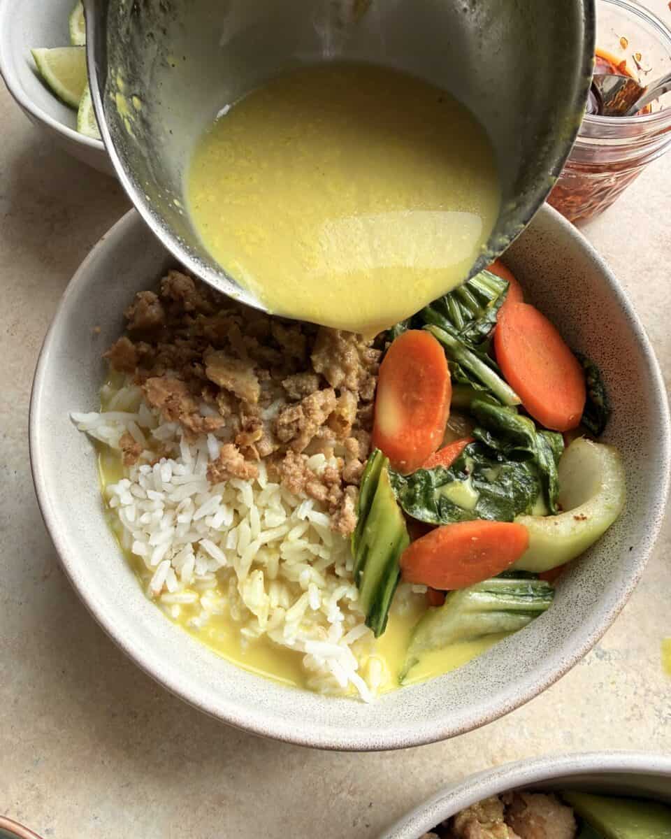 Pouring golden coconut milk broth over a ground chicken and rice bowl.