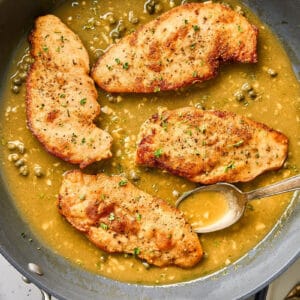 Lemon chicken scallopini in a pan with buttery piccata sauce.