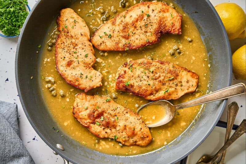 Lemon chicken scallopini in a pan with buttery piccata sauce.