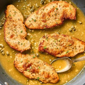 Chicken scallopini in a pan with buttery piccata sauce.