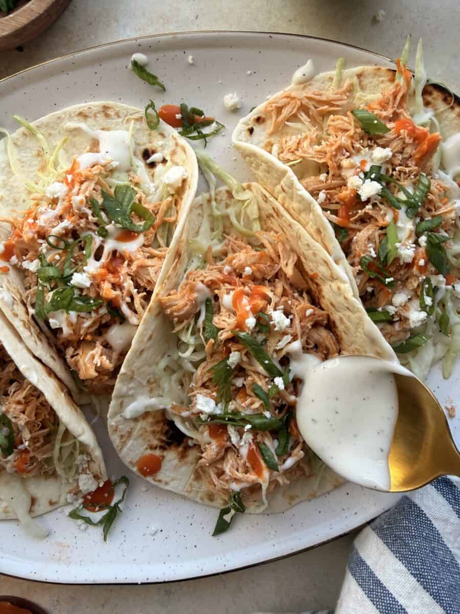 Drizzling ranch over buffalo chicken tacos.
