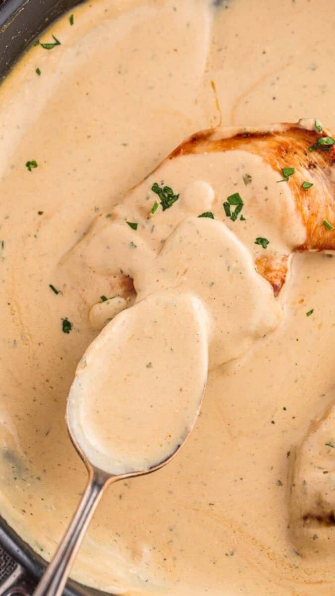 Spooning cream cheese sauce over chicken.