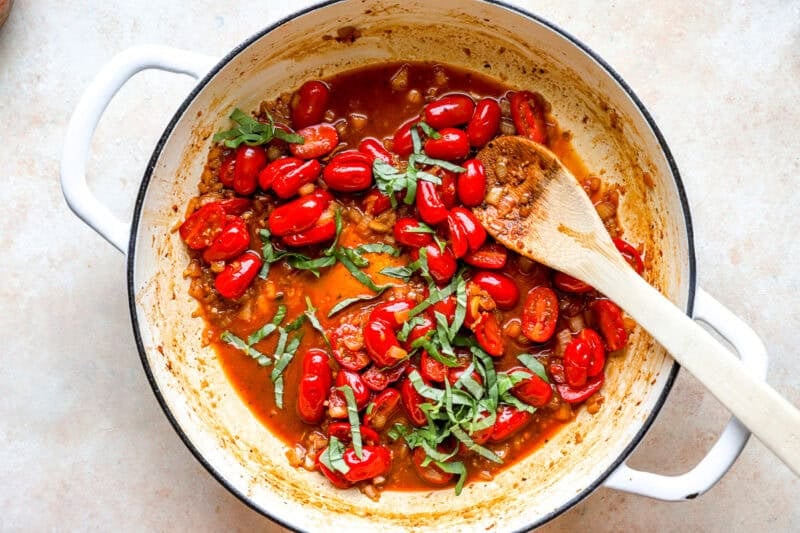 Tomatoes and basil cooking in a pan.