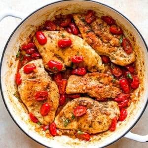 Chicken breasts, tomatoes, and basil cooking in a pan.