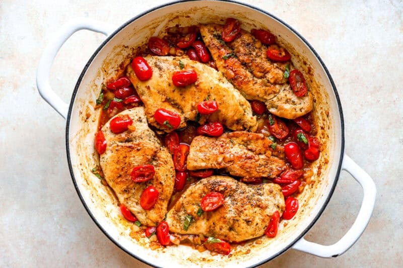 Chicken breasts, tomatoes, and basil cooking in a pan.