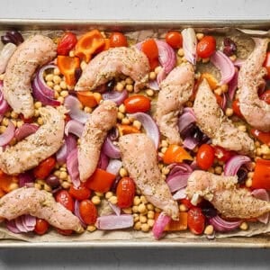 Marinated chicken tenders and veggies in a sheet pan, before roasting.