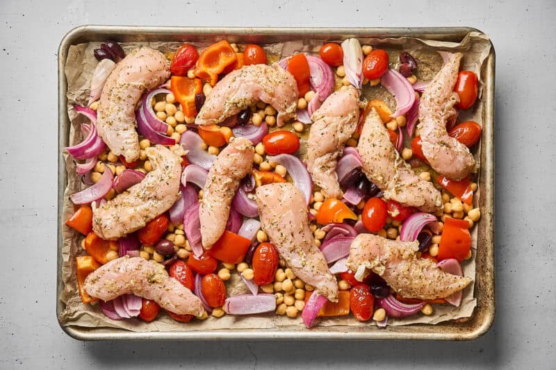 Marinated chicken tenders and veggies in a sheet pan, before roasting.