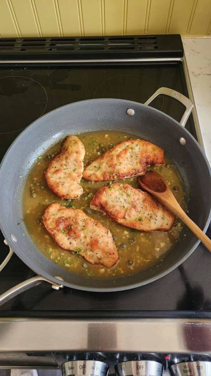 Scallopini chicken cooking in a skillet on the stove.