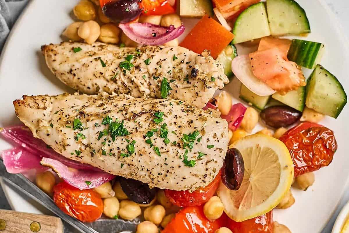 A plate of Greek chicken tenders served with chickpeas and Mediterranean veggies.