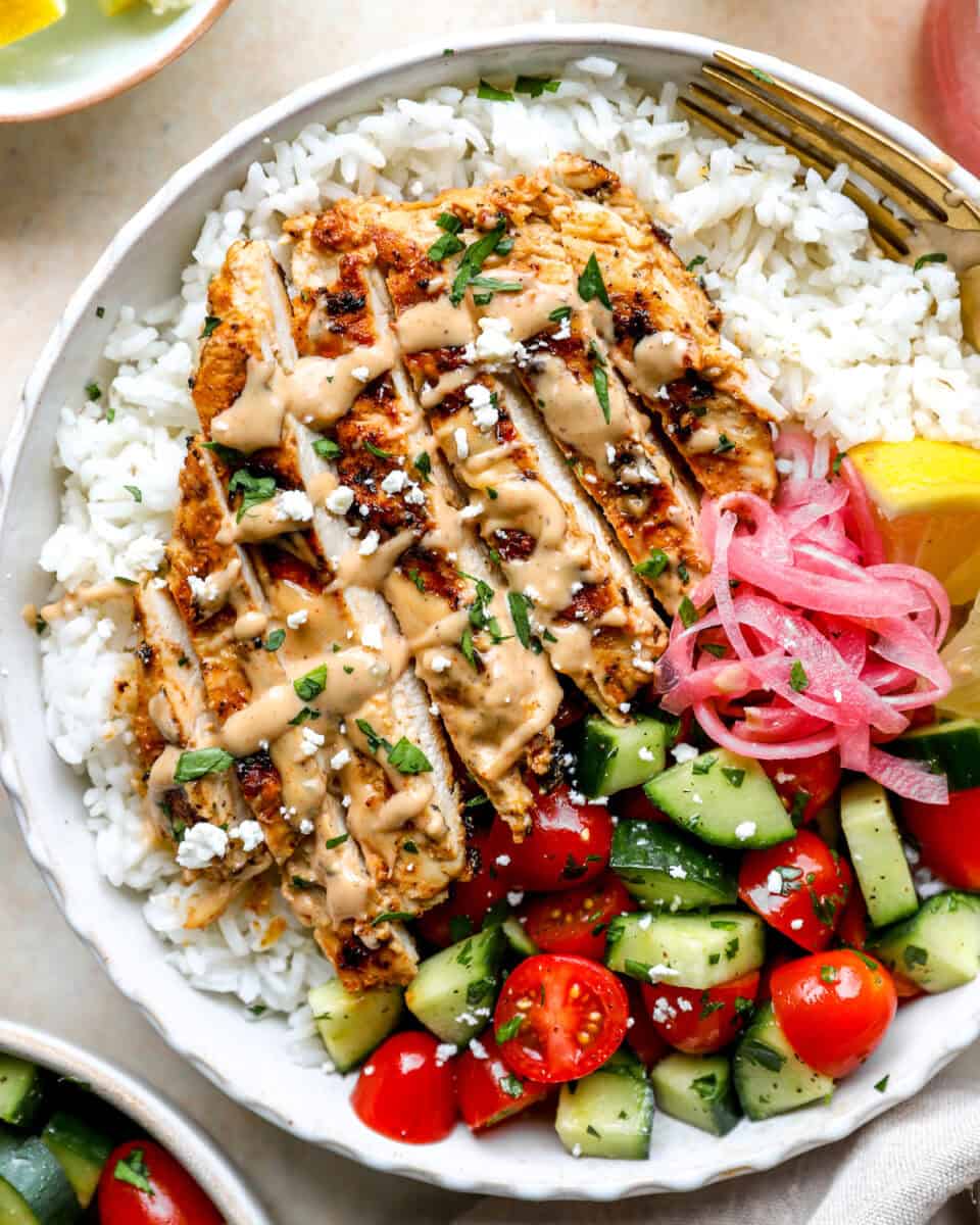 Grilled tahini chicken sliced and served in a bowl of rice and veggies.