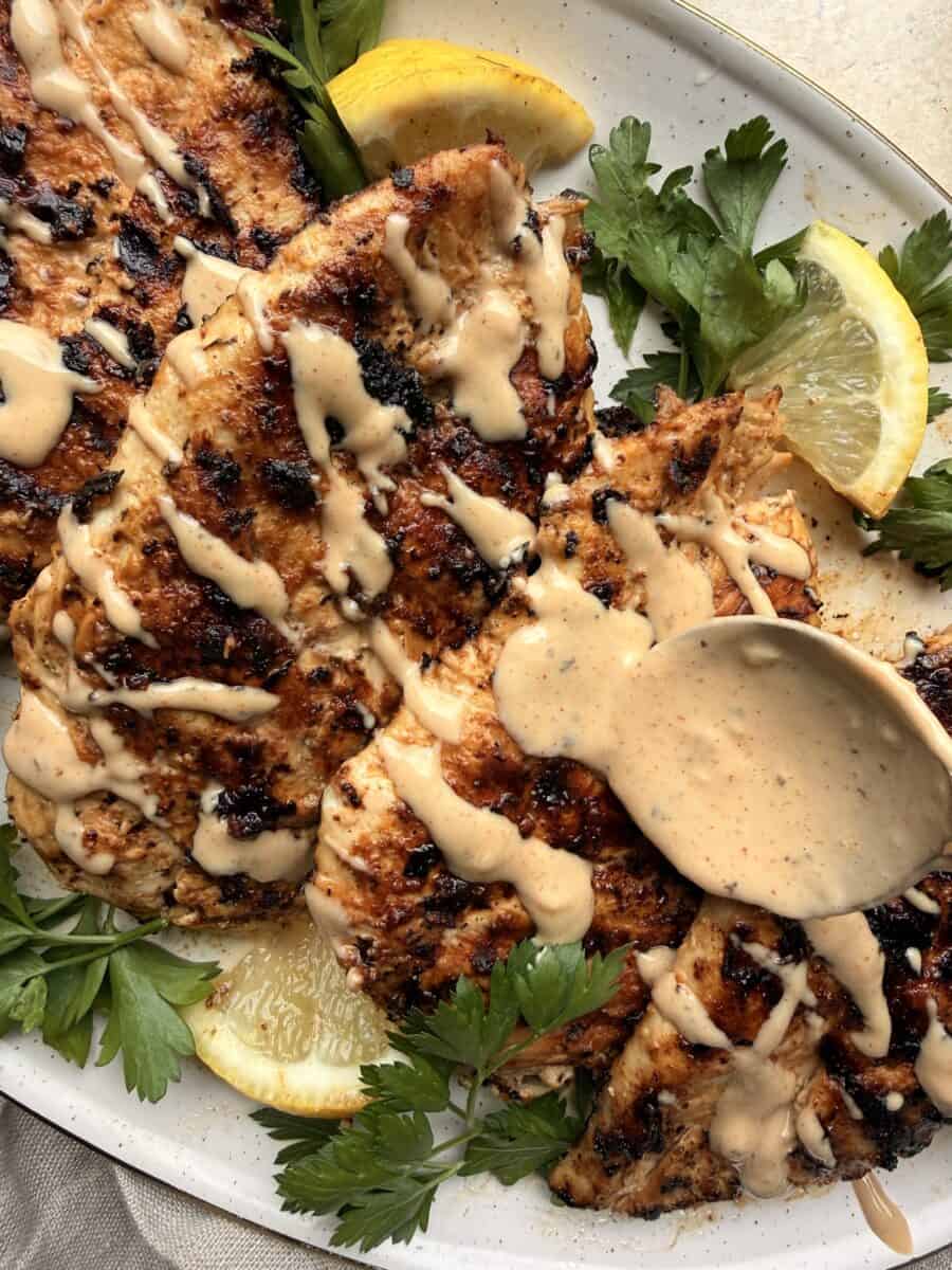 Drizzling homemade tahini sauce over a plate of grilled chicken.