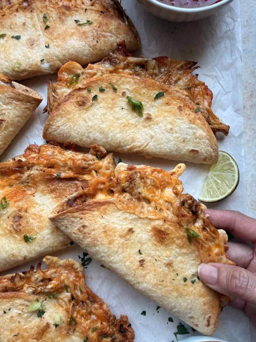 Grabbing a cheesy chicken taco from a baking tray.