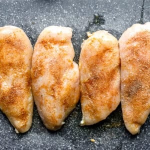 Seasoned chicken breasts lined up on a cutting board.