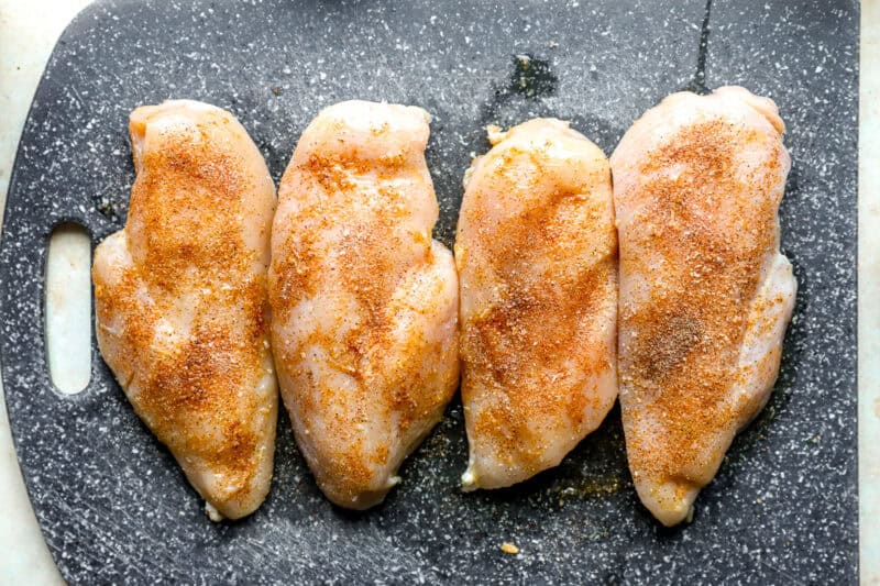 Seasoned chicken breasts lined up on a cutting board.