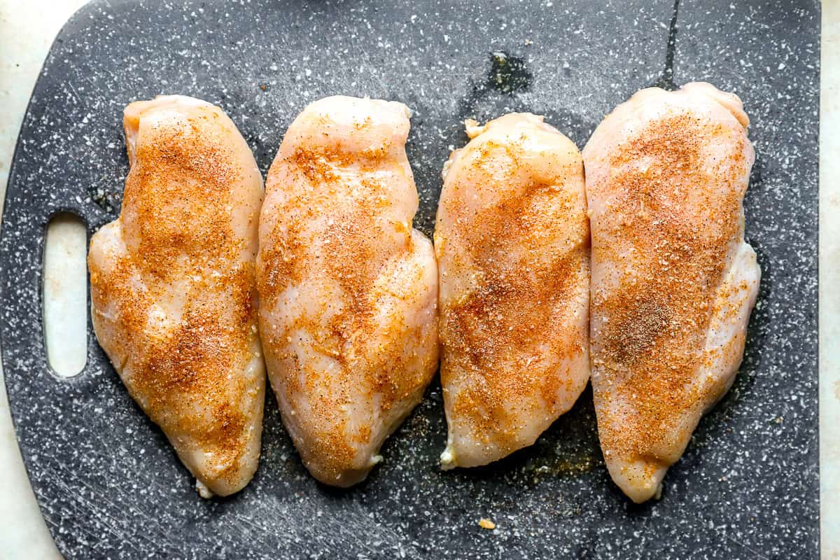 Seasoned chicken breasts lined up on a cutting board.
