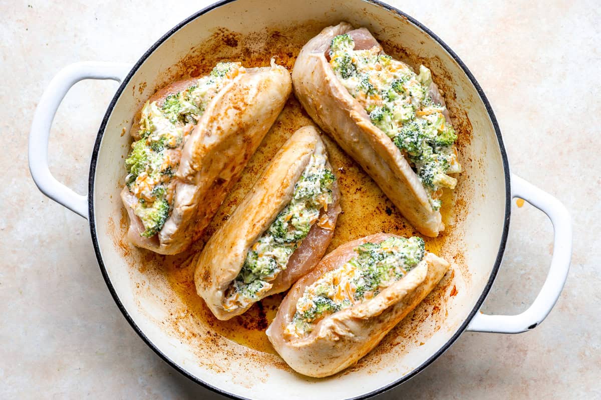 Broccoli stuffed chicken breasts cooking in a pan.