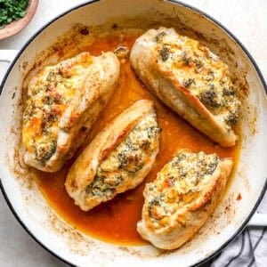 Cooked broccoli cheese stuffed chicken breasts in a pan.