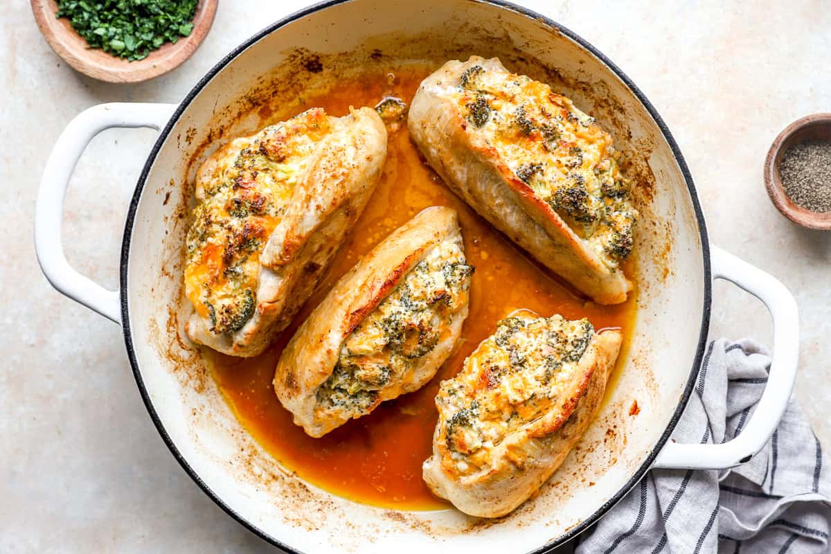 Cooked broccoli cheese stuffed chicken breasts in a pan.