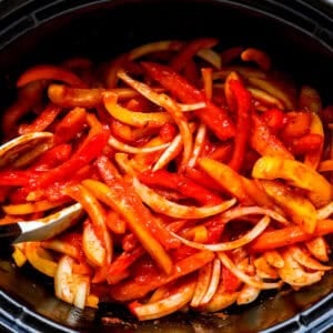 Sliced bell peppers and onions in a slow cooker.