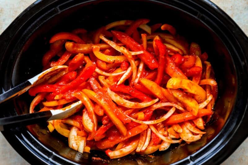 Sliced bell peppers and onions in a slow cooker.