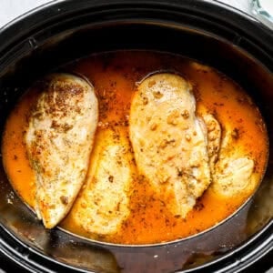 Chicken breasts placed in a slow cooker with a pan sauce.