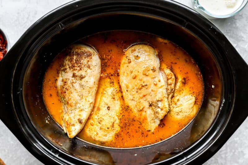 Chicken breasts placed in a slow cooker with a pan sauce.