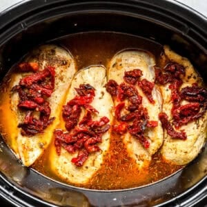 Chicken breasts in a slow cooker, topped with sun-dried tomatoes.